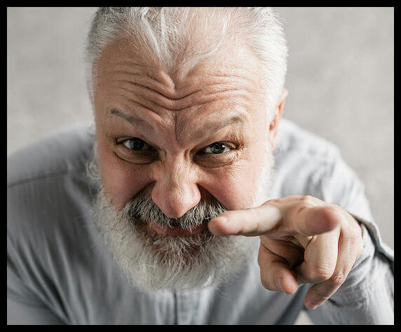 Older man with gray beard pointing intensely at the camera.